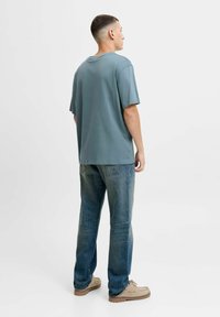 Lyseblå kortærmet t-shirt med løs pasform, sammen med slidte blå straight-leg jeans og beige fodtøj.