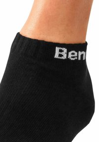 Calcetín negro hasta el tobillo hecho de una tela texturizada, con un diseño acanalado y un logo bordado en blanco en el puño.