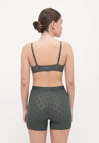 Ensemble de lingerie en maille vert foncé composé d'un soutien-gorge et de shorts. Le soutien-gorge est doté de bretelles réglables et d'un détail en logo. Les shorts présentent une texture à motif avec une taille lisse.
