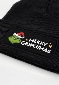 Black knit beanie featuring an embroidered patch with a green character wearing a red Santa hat and the text "MERRY GRINCHMAS" in bold white letters.