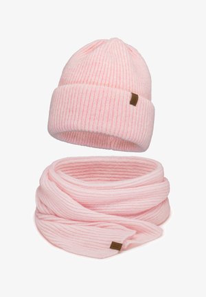 Világos rózsaszín bordázott kötött sapka és hozzá illő végtelen sál, mindkettőn egy kisebb barna márkacímke fehér háttérrel.