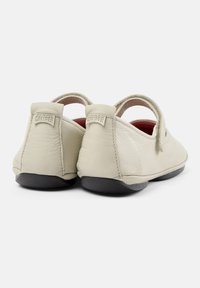 Scarpe in pelle beige chiaro con un design arrotondato, dotate di una suola in gomma nera e una fascia sul tallone posteriore con dettagli del logo.