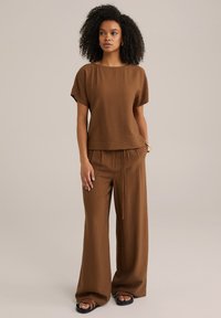Hnědý texturovaný top s krátkým rukávem a volnými hnědými kalhotami. Outfit má pas na stažení a ploché černé sandály.