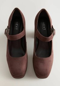 Pantofi Mary Jane din suede maro, cu vârf rotund, curea ajustabilă și platformă joasă. Suprafață texturată și logo pe brant.