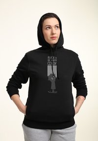 Felpa nera con cappuccio realizzata in tessuto morbido, caratterizzata da una stampa grafica con testo e design bianchi. Include una tasca a marsupio e cordini.