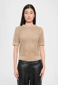 Maglia a manica corta con scollo rotondo in oro con motivo a punto aperto. Abbinata a pantaloni in pelle nera. Tessuto leggero e con texture.