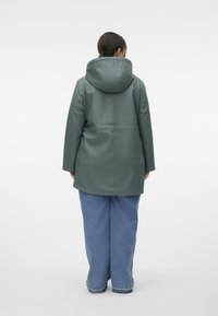 Green waterproof coat with a hood, featuring a relaxed fit and a smooth texture. Worn over light blue wide-leg jeans.