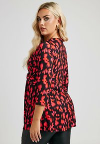 Top a maniche tre quarti con motivo rosso e nero, scollatura aderente e orlo svasato. Tessuto liscio, leggero.