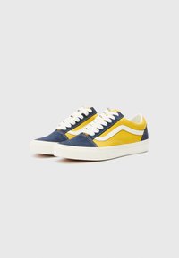 Sneakers with navy blue and yellow canvas upper, white accents, round toe, and white laces. Rubber sole with textured details.