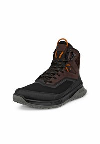 Scarpa alta nera e marrone con pannelli in rete e pelle, dettagli arancioni e suola testurizzata. Presenta occhielli rinforzati e un sistema di allacciatura.
