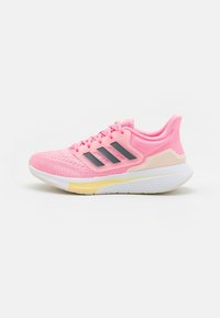 Juoksukengät, joissa on vaaleanpunainen verkko-osa, mustat raidat, valkoinen välipohja ja keltaisia yksityiskohtia. Varustettu tekstuuripinnalla ja pehmustetulla nilkkaremmillä.