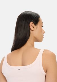 Light pink tank top with wide straps and a scoop neckline, featuring a silver accent at the back. Soft fabric with a smooth texture.