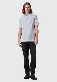 Lys grå polo med tre knapper, korte ermer og en subtil logo. Kombinert med svarte jeans og svarte støvler.