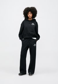 Μαύρο φούτερ με κουκο ύλα, μπροστινή τσέπη και λογότυπο, σε συνδυασμό με φαρδιά μαύρη φόρμα με ελαστική μέση και λογότυπο. Λεπτή υφή από βαμβάκι.