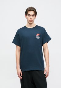 Σκούρο ναυτικό μπλε βαμβακερό T-shirt με στρογγυλή λαιμόκοψη. Διαθέτει τοπικό κόκκινο λογότυπο της Nike και κείμενο "ΑΠΟΚΛΕΙΣΤΙΚΑ ΓΙΑ ΕΞΟΥΣΙΟΔΟΤΗΜΕΝΟ ΠΡΟΣΩΠΙΚΟ" στο αριστερό στήθος.