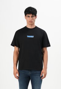 Zwarte katoenen T-shirt met een ronde hals, korte mouwen, voorzien van een blauw "Tommy Jeans" logo op de voorkant. Draagt met blauwe spijkerbroeken.