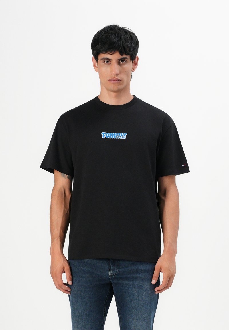 Črna bombažna majica s krožnim izrezom, kratkimi rokavi, z modrim logotipom "Tommy Jeans" na sprednji strani. Oblečena z modrimi kavbojkami.