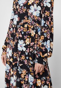 Svart blommig klänning med lösa långa ärmar, prydd med stora blå och orange blommor, samlad midja och flödande lagerkjol.