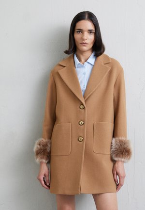 Cappotto in misto lana marrone con grandi tasche frontali, quattro bottoni e dettagli in pelliccia sulle maniche. Presenta un colletto a scomparsa e una vestibilità dritta.
