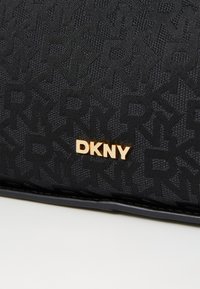 Czarna torba z tkaniny o teksturowanym wzorze, z logo DKNY w złotym metalu. Gładkie wykończenie z krawędziami wykończonymi w czerni.
