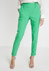Groene tapse broek van gladde stof met een hoge tailleband en opgerolde manchetten. Gekocht met een wit shirt met lange mouwen en zilveren sandalen.
