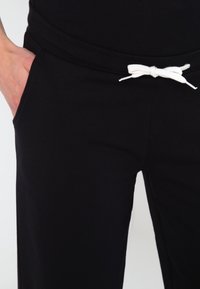 Black sweatpants featuring a white drawstring, side pockets, and a soft texture, suitable for casual wear or exercise.