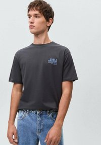 Gray short-sleeve t-shirt with a crew neck and blue printed graphic "FUEL & GARAGE" on the chest, paired with light blue denim jeans.