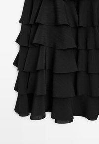 Black layered dress with ruffled tiers, textured fabric, and a smooth finish. Features cascading waves and a slight sheen throughout.