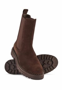 Brązowe zamszowe botki za kostkę z elastycznymi panelami bocznymi i grubymi podeszwami, jeden but stoi w pionie, a drugi leży płasko obok niego.