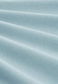 Helles blaues Gewebe mit einer weichen, glatten Textur, das mehrere subtile Falten oder Wellen aufweist und ein sanftes, fließendes Erscheinungsbild erzeugt.