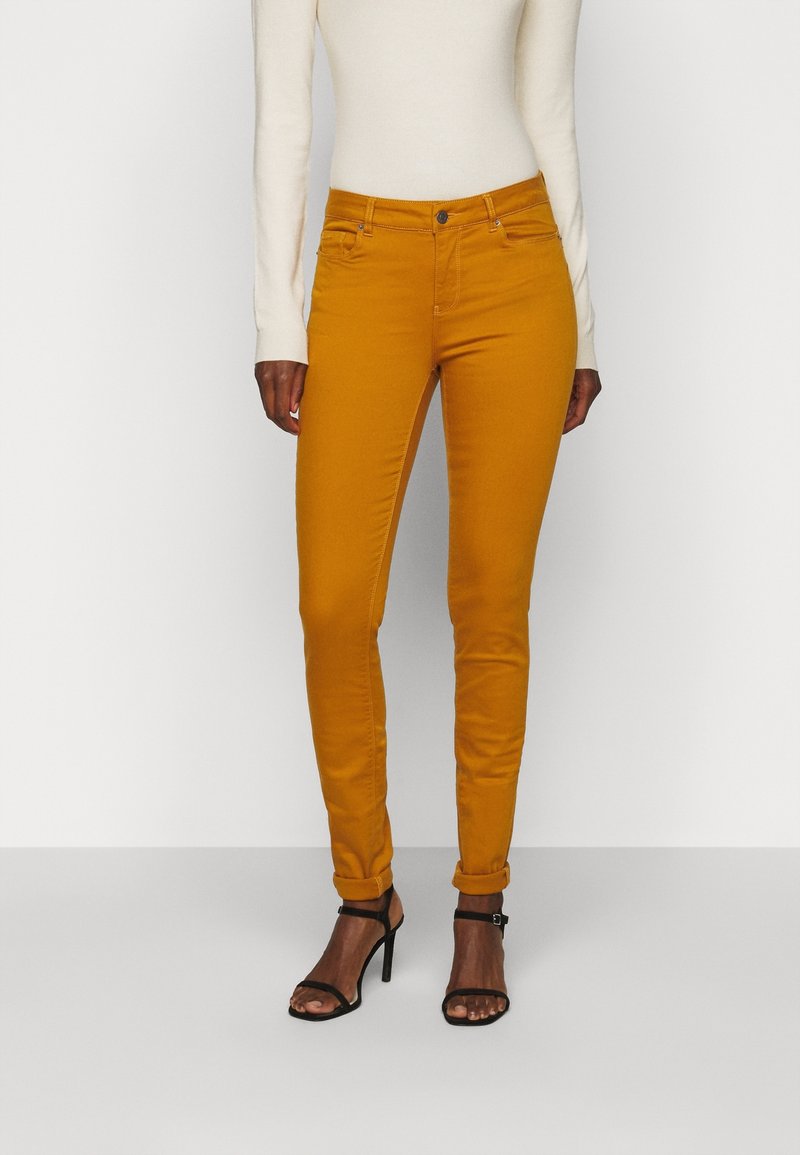 Gula smala jeans med en figurnära design och uppvikta fållar, tillverkade av en blandning av bomull. Matchas med svarta sandaler med remmar.