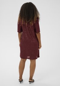 Bordo haljina sa šljokicama, kratkim rukavima, do koljena, s oblikovanim siluetom i teksturiranom površinom. Uparen s crnim sandalama na visoku petu.