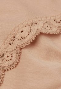 Perzik kleurige stof met ingewikkelde beige kantafwerking die is voorzien van een gegolfde rand en een delicate opengewerkte patroon, dat de zachte textuur en glans benadrukt.