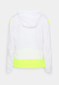 Giacca bianca con cappuccio caratterizzata da un accento giallo neon all'orlo e alla spalla, realizzata in un tessuto leggero e testurizzato. Visuale dal retro.