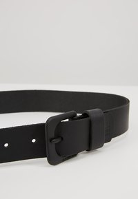 Schwarzer Ledergürtel mit matter Schnalle und verstellbaren Löchern. Das Design ist schlank mit einer glatten Textur und minimalen Details.