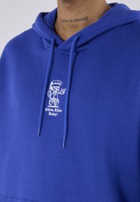 Hoodie bleu en tissu mélangé coton avec une capuche à cordon. Présente un graphique d'un personnage de dessin animé avec le texte "Slice, Slice Baby!" en blanc.