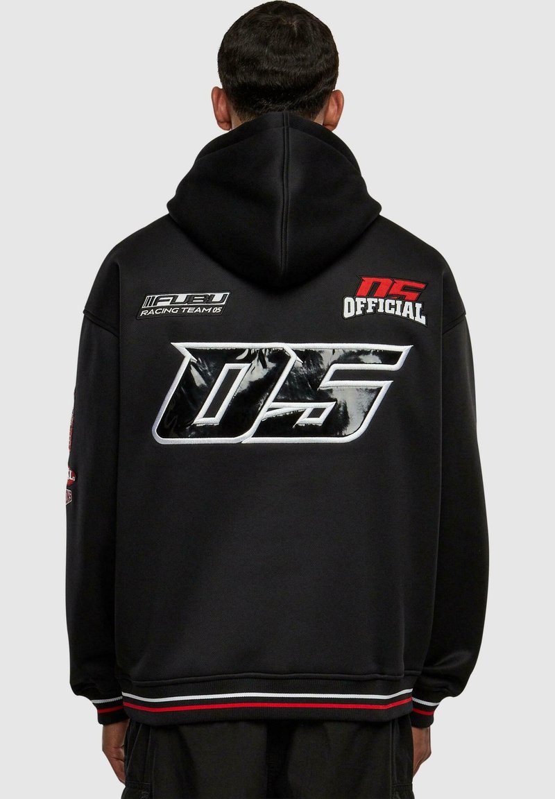 Schwarzer Kapuzenpulli mit einem großen silbernen Grafik-Logo auf der Rückseite, das Text und Patches zeigt. Enthält rot-weiße gestreifte Akzente an den Ärmeln.
