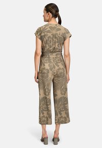 Combinaison légère marron clair avec des jambes larges, des manches courtes et un motif floral. Le tissu est doux, avec une taille ceinturée et une coupe décontractée.