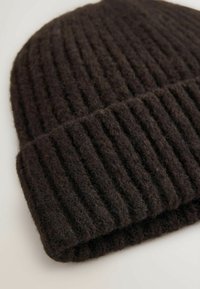 Brun strikket beanie-hat lavet af uld, med ribbet tekstur og ombuk. Materialet ser blødt og fuzzy ud.