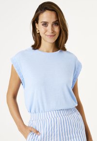 Haut bleu clair à manches courtes avec des détails en œillets aux épaules, associé à un bas rayé taille haute. Tissu doux, coupe décontractée.