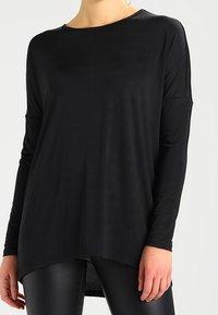 Schwarzes Langarmshirt aus glattem Stoff, mit lockerer Passform, runder Ausschnitt und abgerundetem Saum hinten.