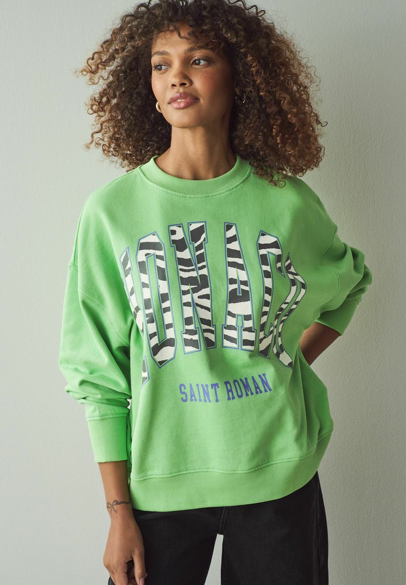 Groene sweatshirt met grote, vetgedrukte letters in zebrastreep. Heeft een ronde hals, een ontspannen pasvorm en geribde manchetten. Gaat gepaard met zwarte broek.