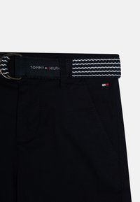 Námořnické kalhoty s tkaným pásem zdobeným vzorem bílých vln. Pas je opatřen kovovou sponou a logem Tommy Hilfiger.