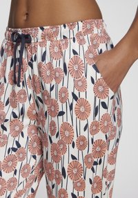 Närbild av en hand i fickan på vita byxor med ett blomster mönster i rosa och marinblått, samt en marinblå snörning i midjan.