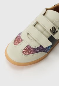 Zapato de cuero crema con doble tira de velcro, con un degradado brillante en rosa, púrpura y azul en el costado y suela de goma.