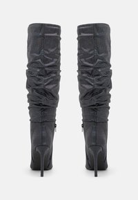 Botas pretas até ao joelho com textura franzida e saltos altos em agulha. Apresentam fecho zip na parte de trás e material suave e brilhante.