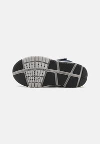 Suela de zapatilla con un diseño de goma texturizada en negro y gris, que presenta un dibujo de la banda de rodadura para tracción y secciones ahuecadas para flexibilidad.