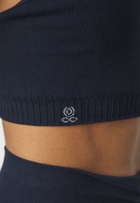 Soutien-gorge de sport en tissu côtelé marine avec une finition texturée. Il présente une bande inférieure tricotée et un détail de logo blanc à l'ourlet.