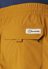 Yellow fabric shorts with an elastic waistband and a back pocket featuring a flap, secured by a button, labeled "berghaus" in white.