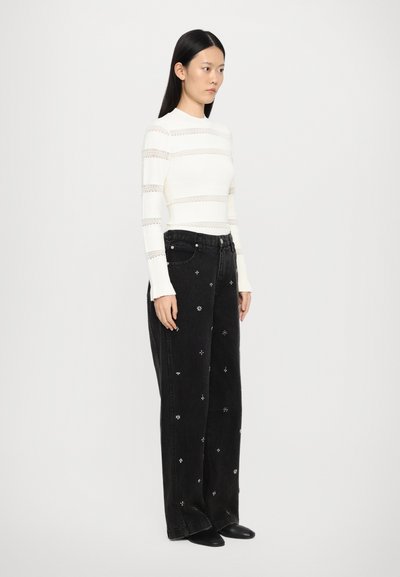 White long-sleeve shirt with lace stripes, paired with black wide-leg jeans featuring floral embroidery, and ankle boots.